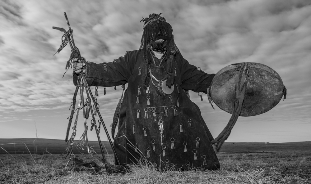 A Mongolian shaman in ceremonial dress, standing on the open steppe.